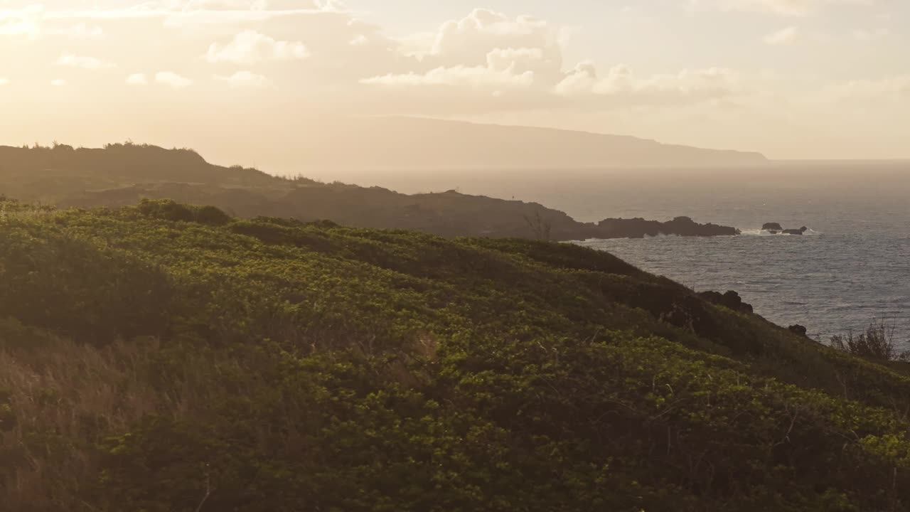 太阳落在毛伊岛西北海岸郁郁葱葱的绿色悬崖和宁静的海洋上视频素材