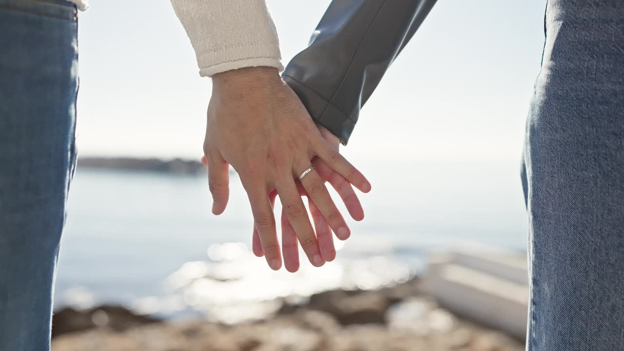 一个男人和一个女人在海边牵手，在宁静的海滩环境中象征着爱和陪伴。视频素材