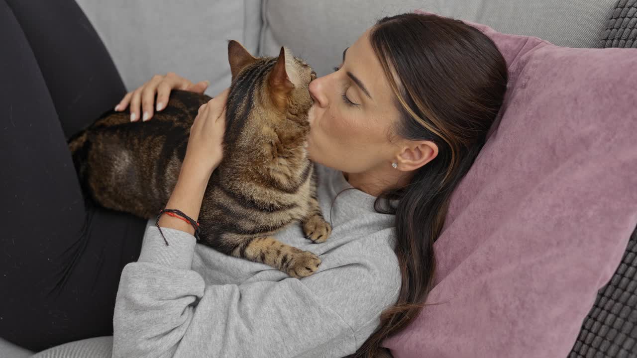 年轻女子和她的宠物猫在家里的沙发上放松，在舒适的客厅里享受安静的时刻。视频素材