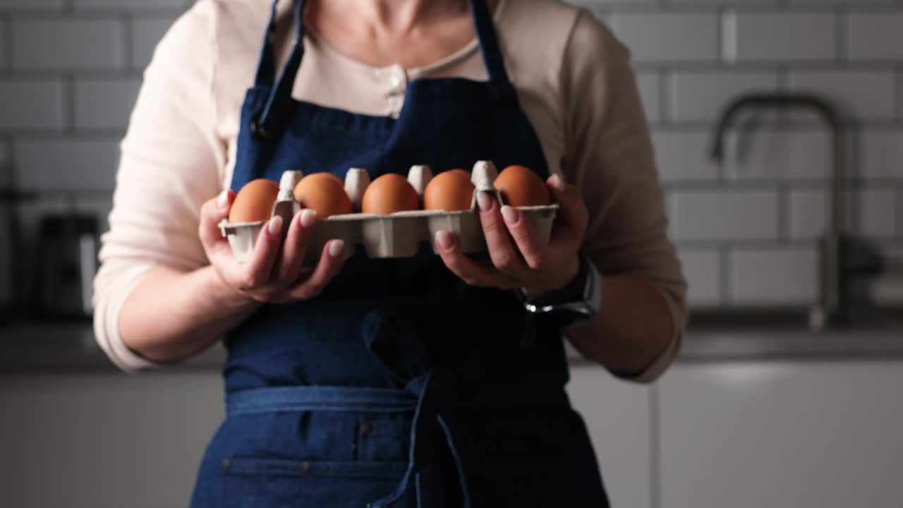 穿围裙的女人展示厨房里的鸡蛋盘视频下载