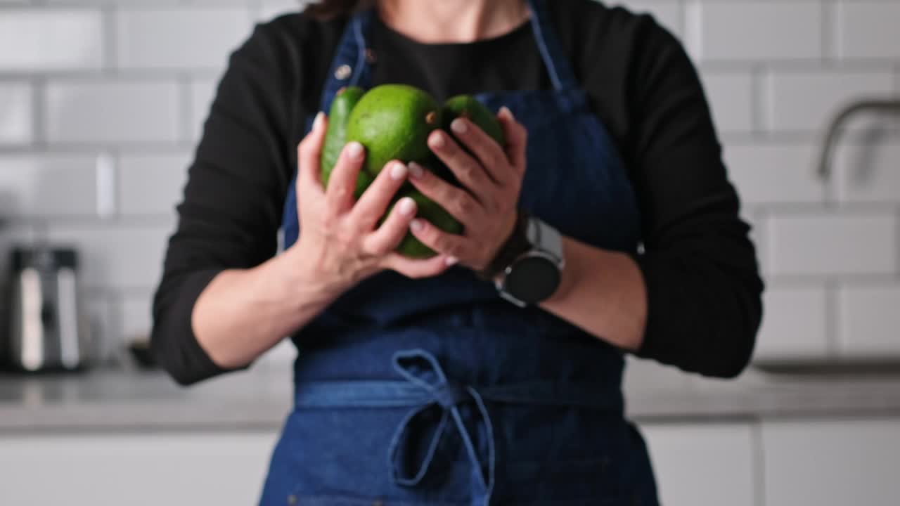 厨房里穿着围裙的女人手里拿着新鲜的绿色鳄梨视频下载