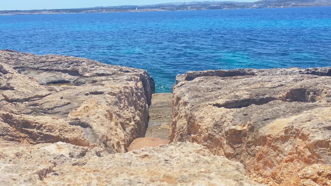 科米诺岛海岸石头上的一个切口，远处是蓝色的地中海和马耳他岛视频素材