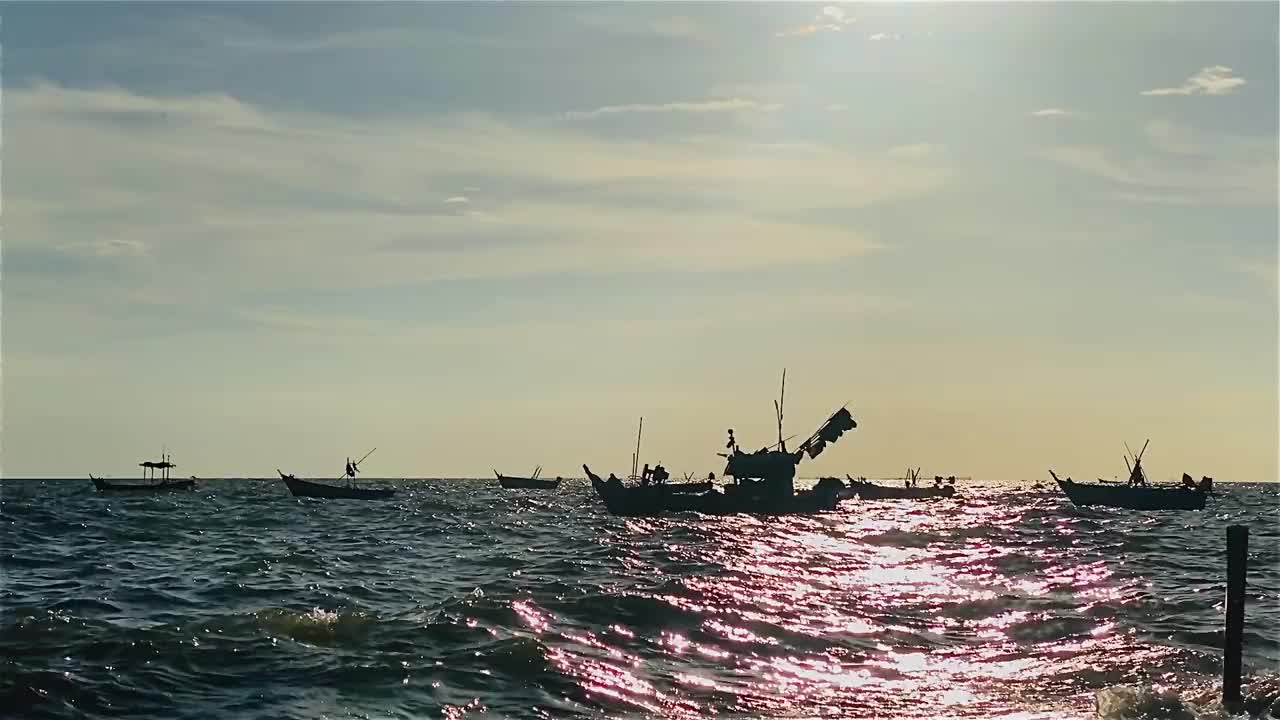 日落时的渔船在海滩风景，日出或日落时的渔船，太阳在云上闪烁，天空和云有力量激发敬畏或惊奇的感觉视频下载