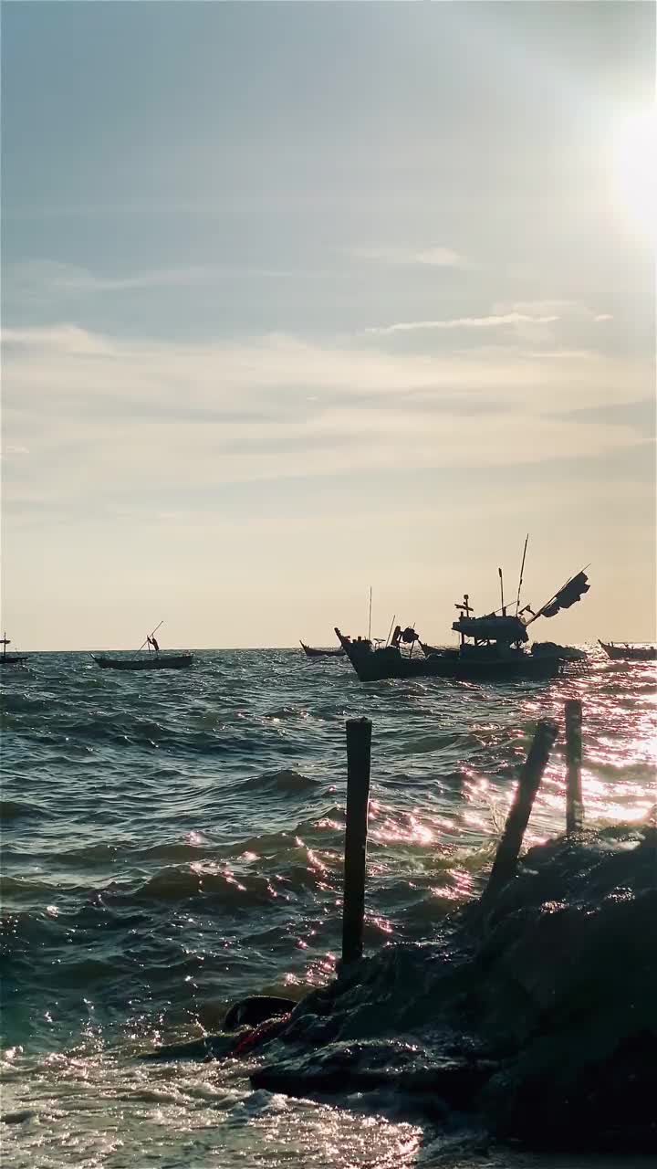 日落时的渔船在海滩风景，日出或日落时的渔船，太阳在云上闪烁，天空和云有力量激发敬畏或惊奇的感觉视频下载