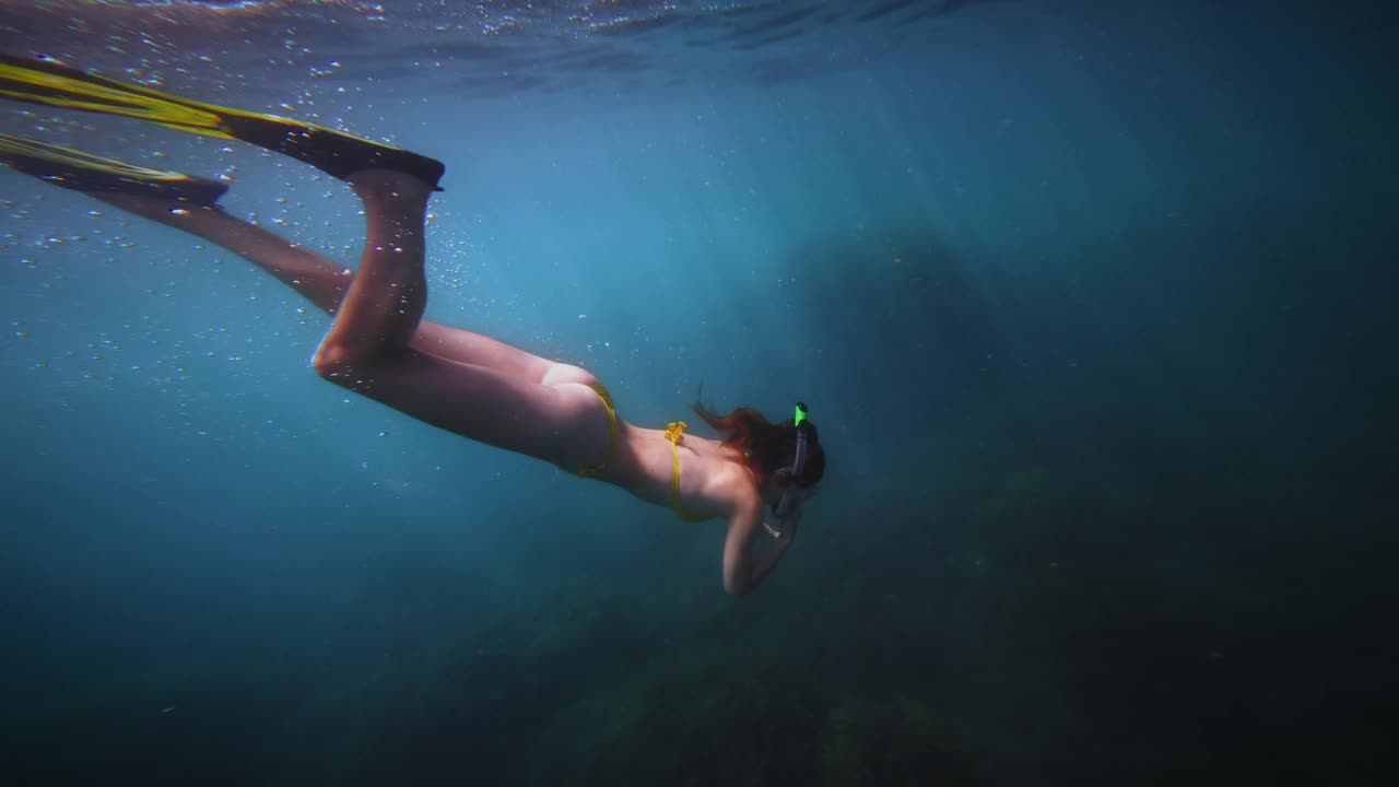 一个女人在清澈的热带海水中浮潜的水下肖像。她正潜到海面以下，以便近距离观察海底的海洋生物视频素材