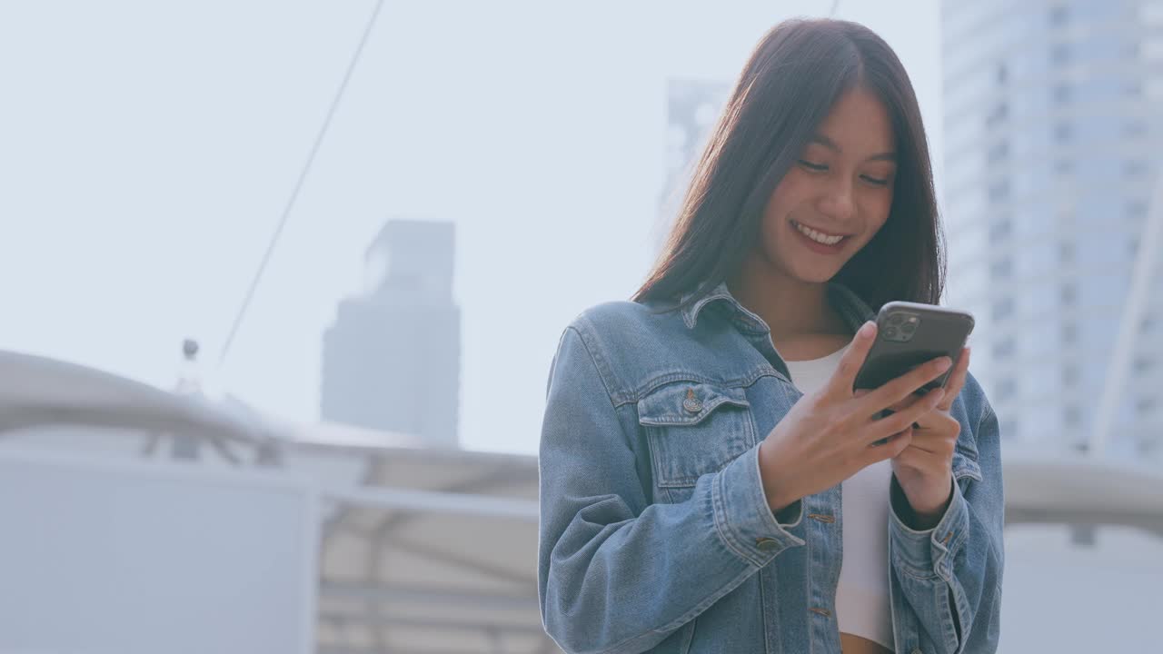 年轻的亚洲女子站在城市里，在街上使用手机视频素材