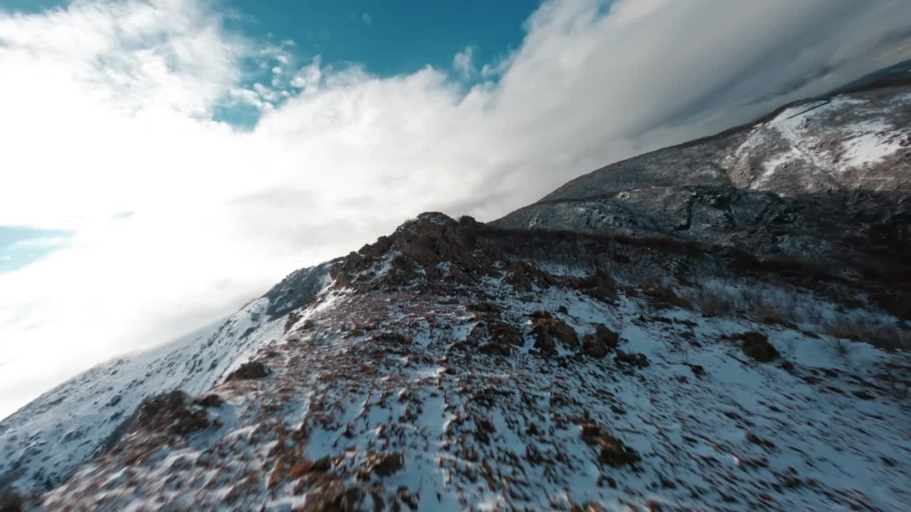 FPV无人机在明亮的天空下飞过白雪皑皑的山峰视频素材