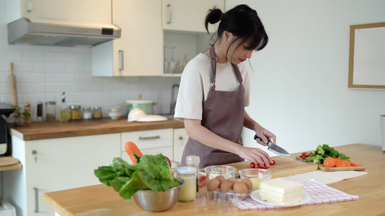 这位亚洲妇女正在厨房切西红柿，准备在家里做亚洲菜视频素材