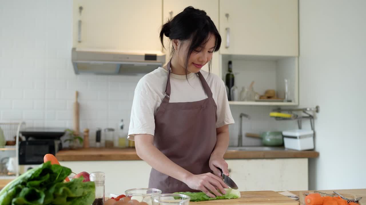 这位年轻的亚洲女子正在厨房里切莴苣，准备在家里做一份亚洲菜视频素材