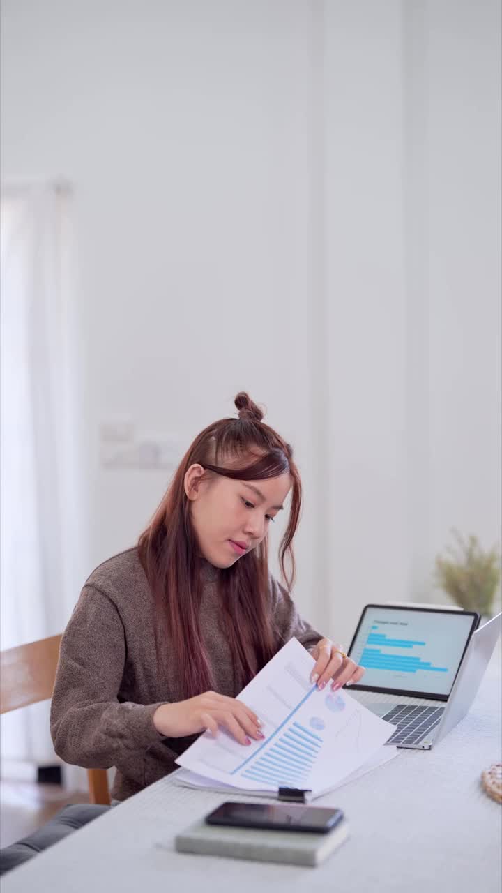 亚洲女商人在家工作，在客厅的桌子上使用她的笔记本电脑视频素材