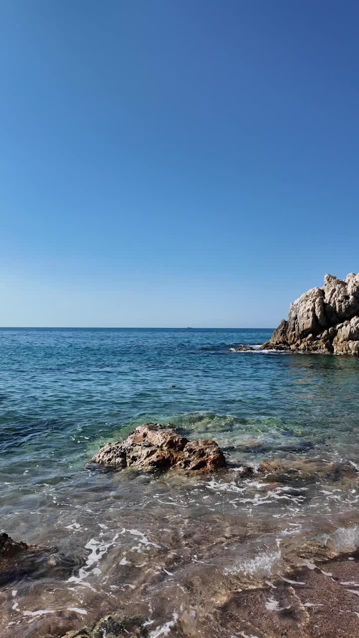 美丽的海景在一个空旷的岩石海滩与蓝天在西班牙，垂直背景视频素材