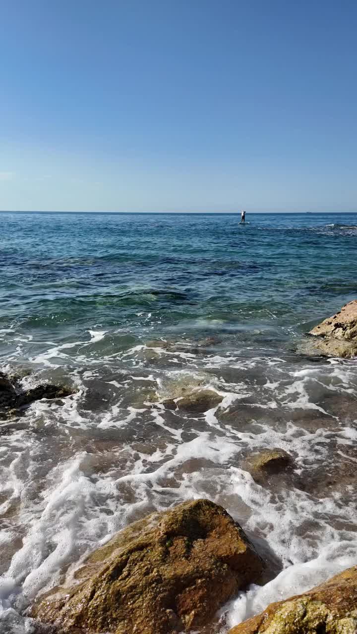 美丽的海景在一个空旷的岩石海滩与蓝天在西班牙，垂直背景视频下载