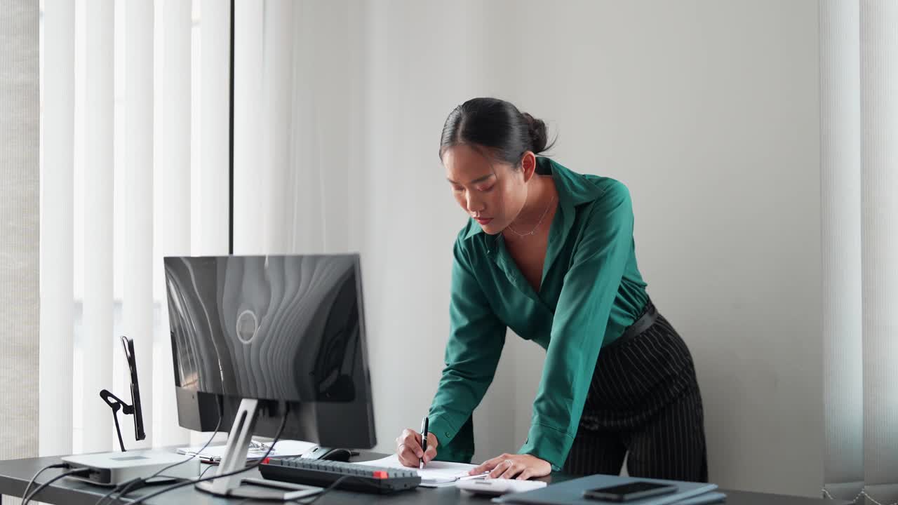 一位亚洲女商人正在办公室里用电脑打字。她热爱职业生活，在自己的办公室里高效地完成任务视频素材