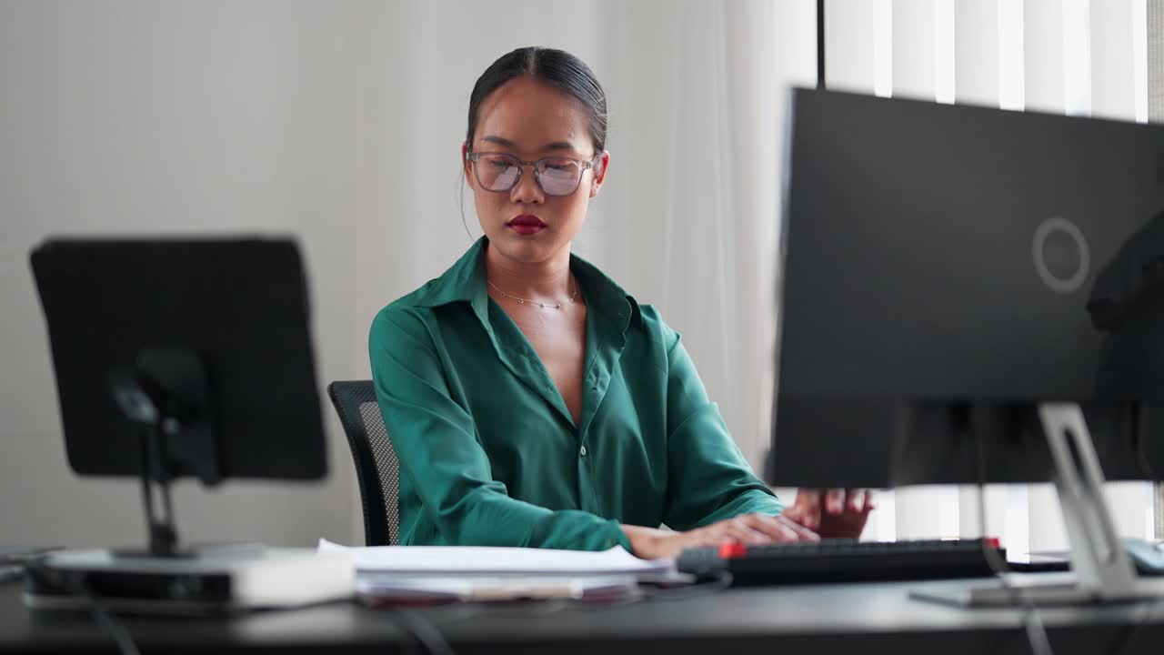 一位亚洲女商人正在办公室里用电脑打字。她热爱职业生活，在自己的办公室里高效地完成任务视频素材