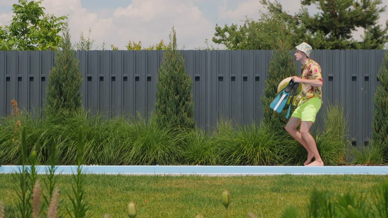 一个快乐的男人带着一个充气戒指和脚蹼在泳池边欢快地跳舞。视频下载