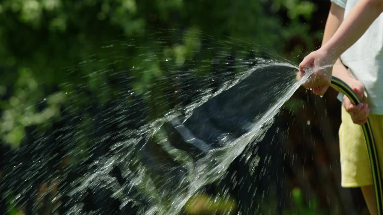 一个女孩在大热天玩花园水管的手。视频下载