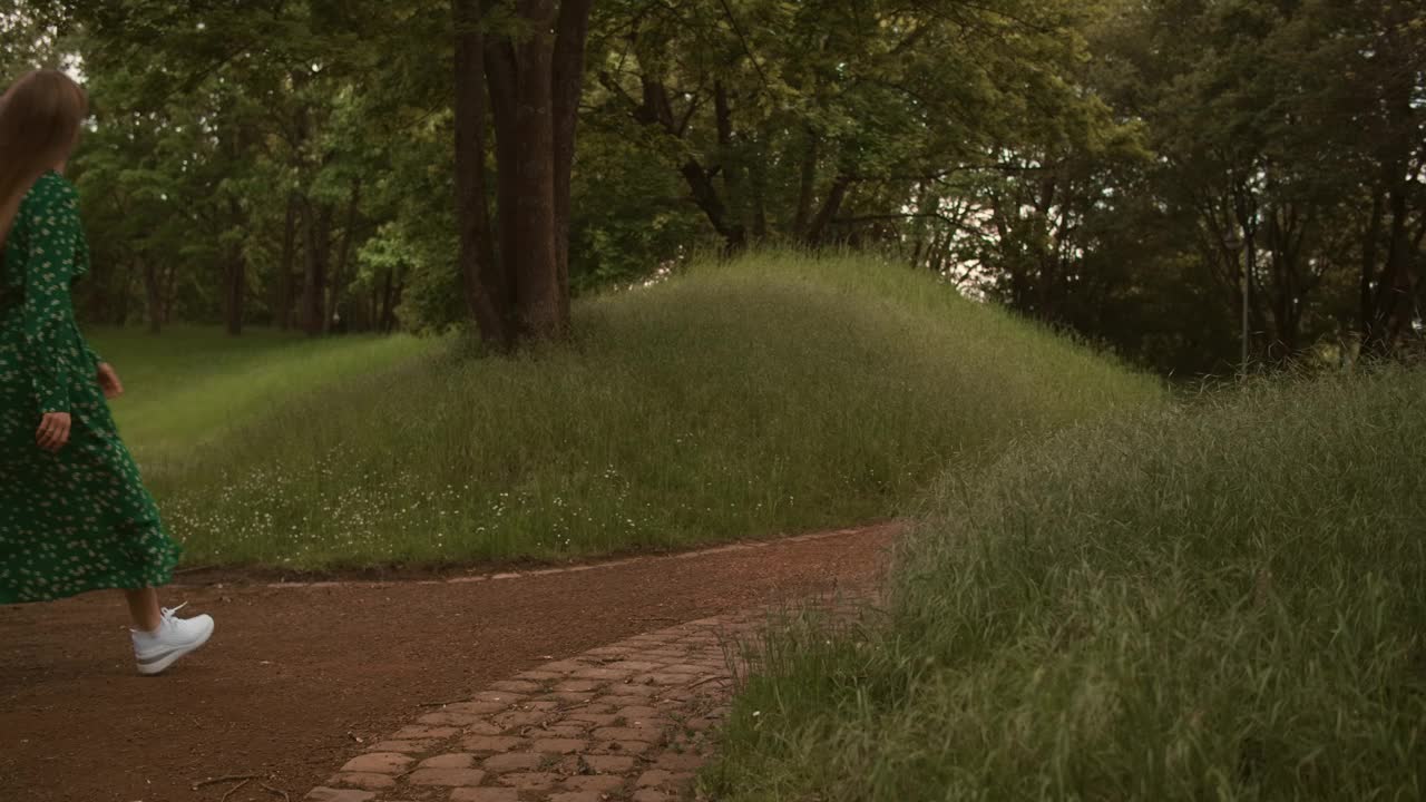 年轻美丽的女人在夏日的大自然中穿着绿色的长裙散步。视频素材