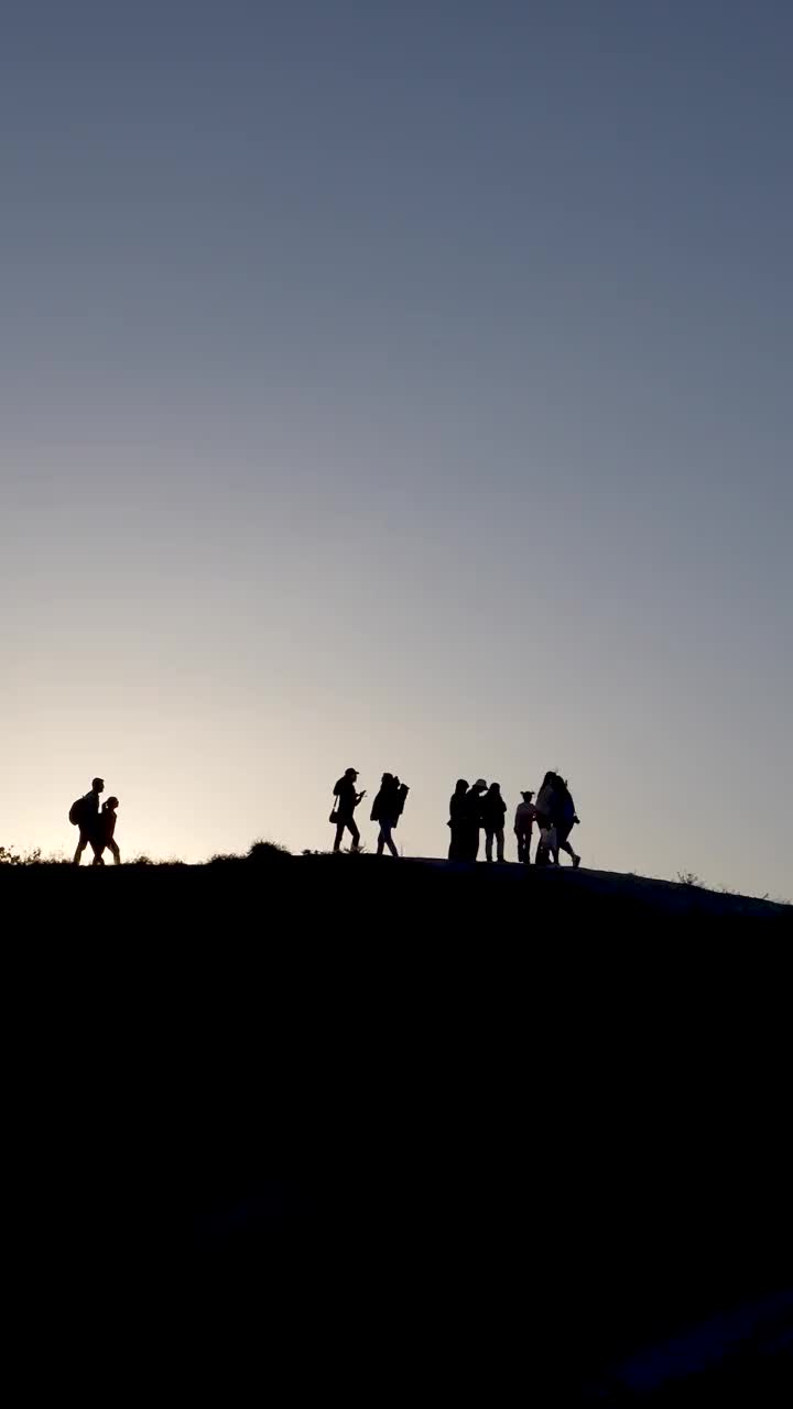 黄昏时分，一群人站在山坡上。山顶上人们的剪影视频素材