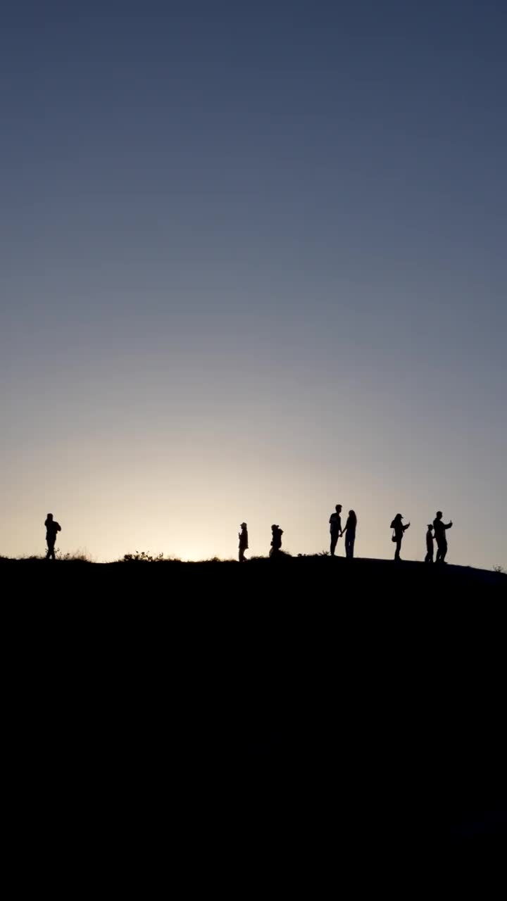 黄昏时分，一群人站在山坡上。山顶上人们的剪影视频下载