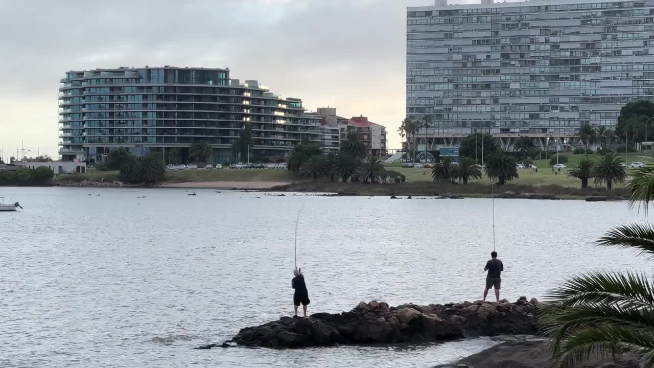 父亲和儿子在日落时分在一个小城市的湖边钓鱼。视频下载