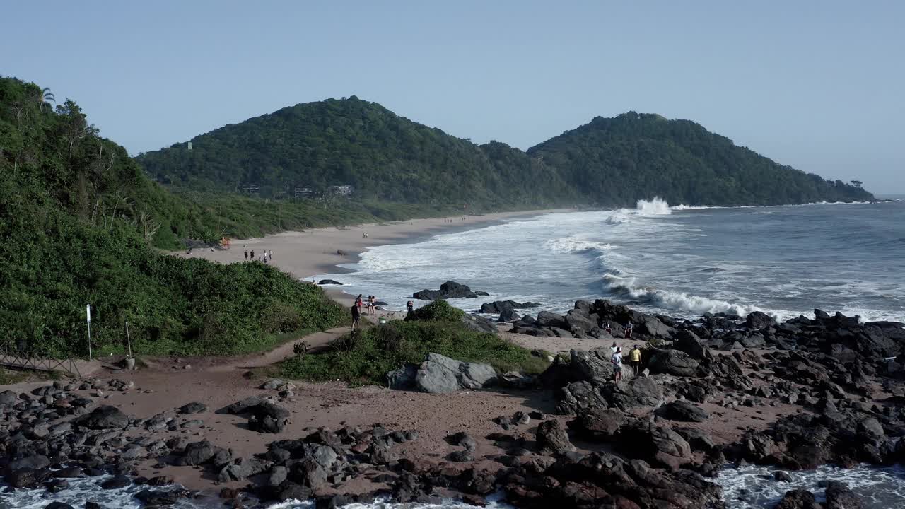 人们在Balneario Camboriu海滩上散步，背景是海浪和悬崖视频素材