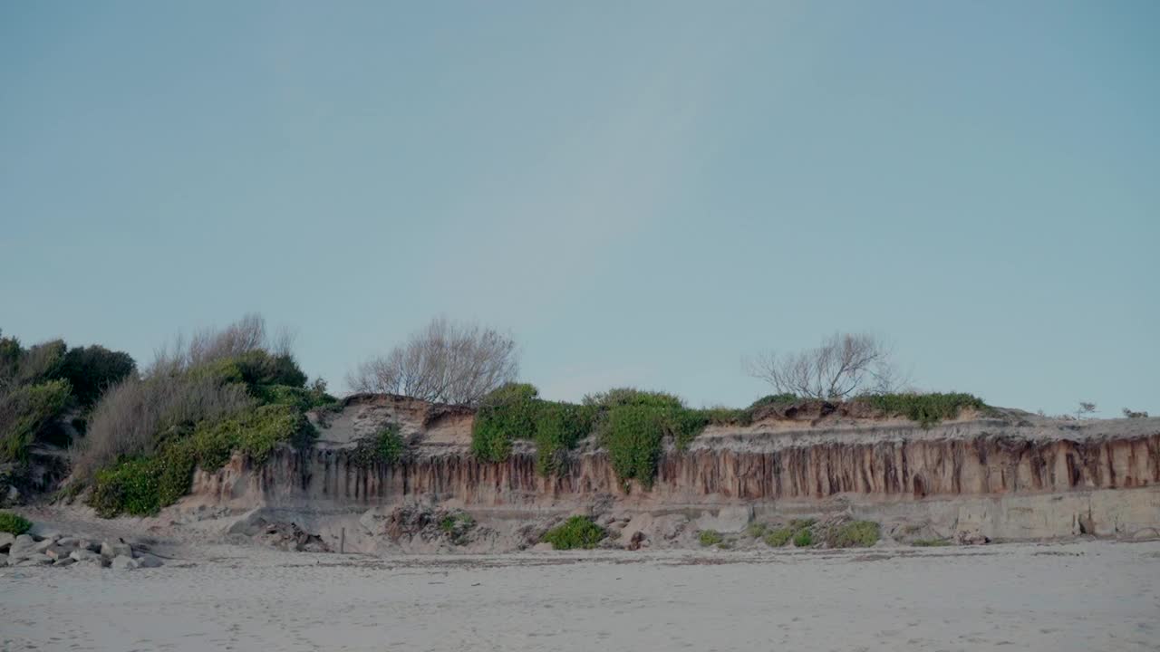 在晴朗的天空下，葡萄牙奥瓦尔的法利西亚海滩上覆盖着植被的海岸悬崖视频素材