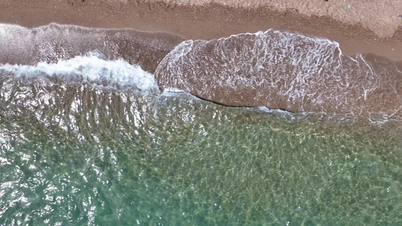 鸟瞰图，一个泡沫的海浪冲击着棕色沙滩和清澈的海水视频素材