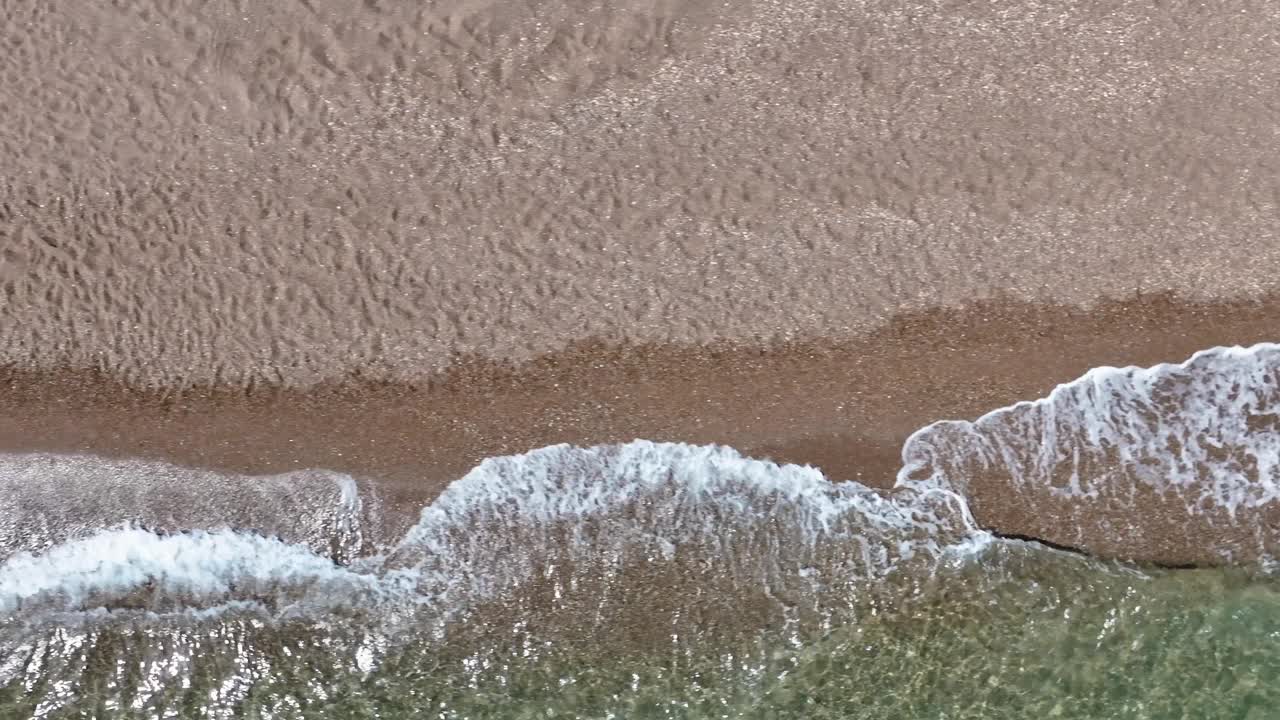 鸟瞰图，一个泡沫的海浪冲击着棕色沙滩和清澈的海水视频素材