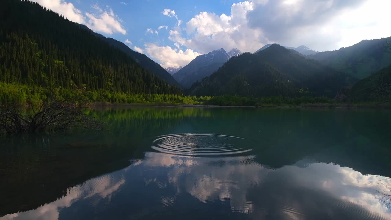 哈萨克斯坦伊塞克山湖，春天清澈的湖水中有美丽的云和山林倒影。视频下载