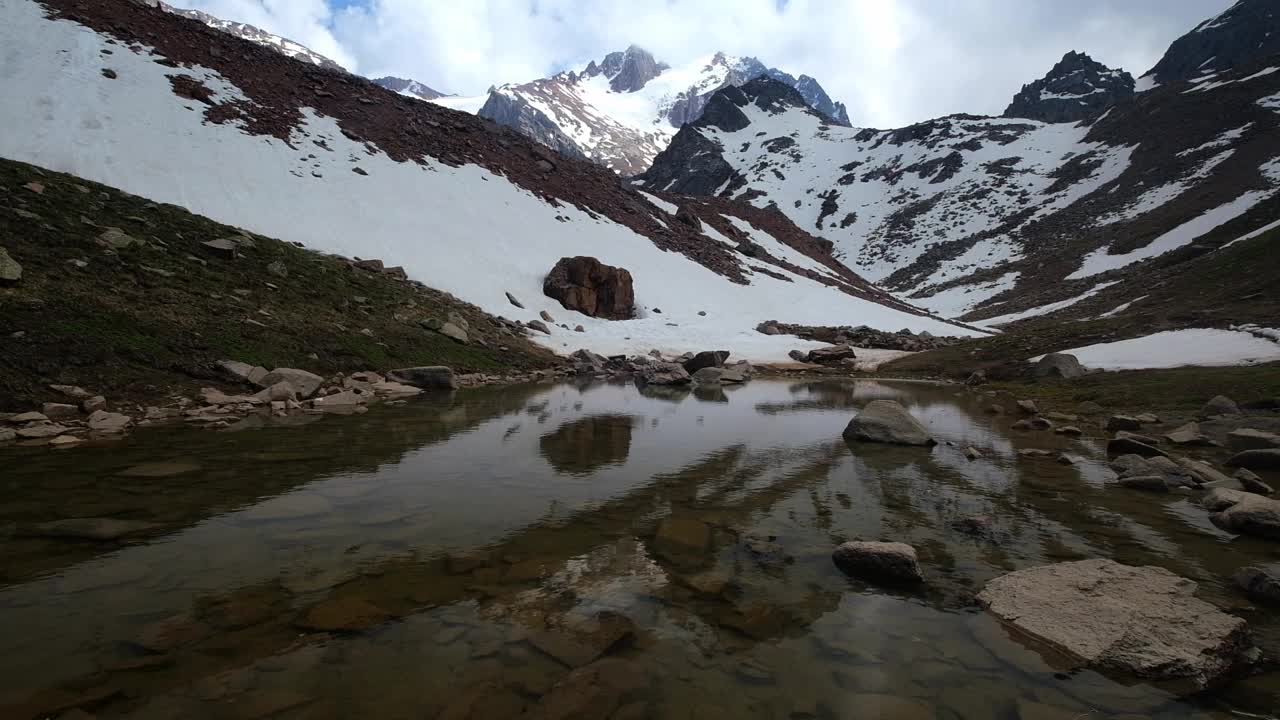 天山高山的冰湖是夏季冰雪融化形成的;山峰、岩石和永恒的冰反射在冰冷的水中。视频下载