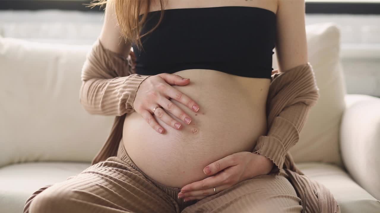 一个孕妇坐着抚摸她的肚子的特写。妈妈要生孩子了。孕妇的肚子。怀孕。母亲的概念。视频素材