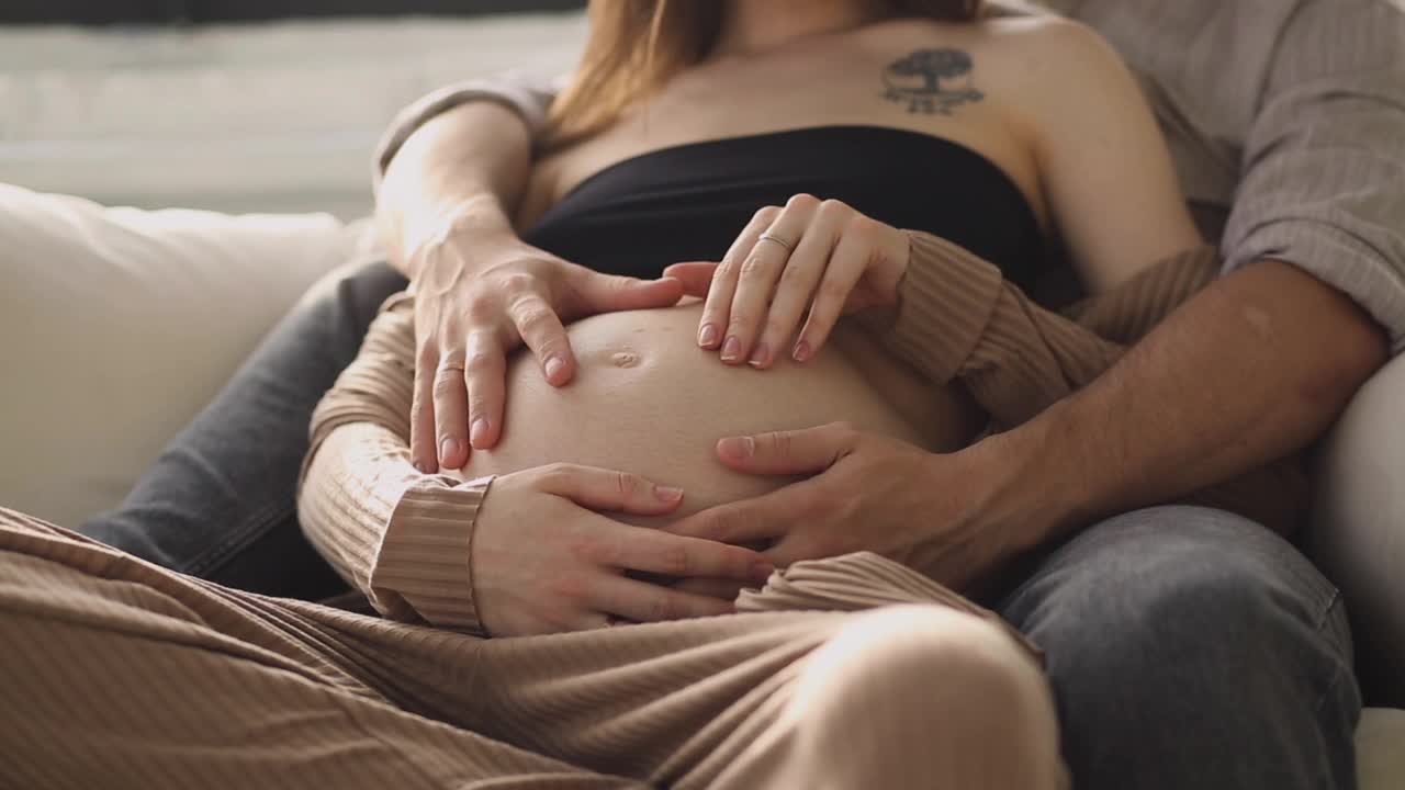 一个丈夫抚摸他妻子怀孕的肚子的特写。体贴的丈夫抚摸着怀孕妻子的肚子。怀孕的幸福。视频下载