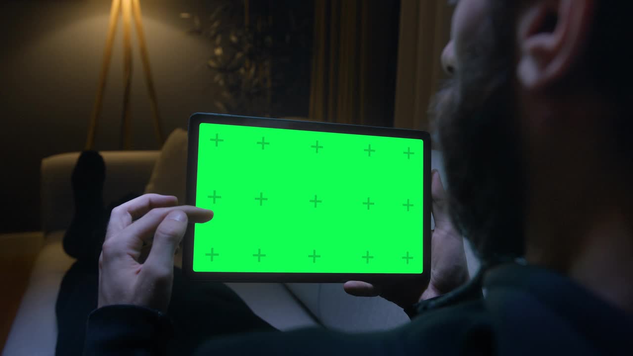 晚上躺在沙发上玩平板电脑，色度键绿色屏幕，浏览社交媒体或网上商店。视频素材