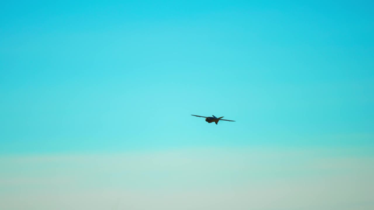 慢动作无人机在天空的背景下飞行。一架飞机形状的无人机正在田野上空飞行。军用无人机。视频下载