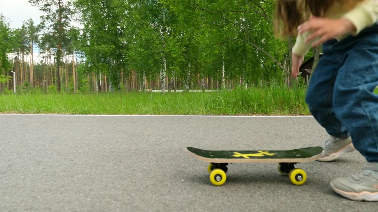 小女孩在柏油路上学习滑板。快乐的女孩在夏天骑滑冰在街上视频素材