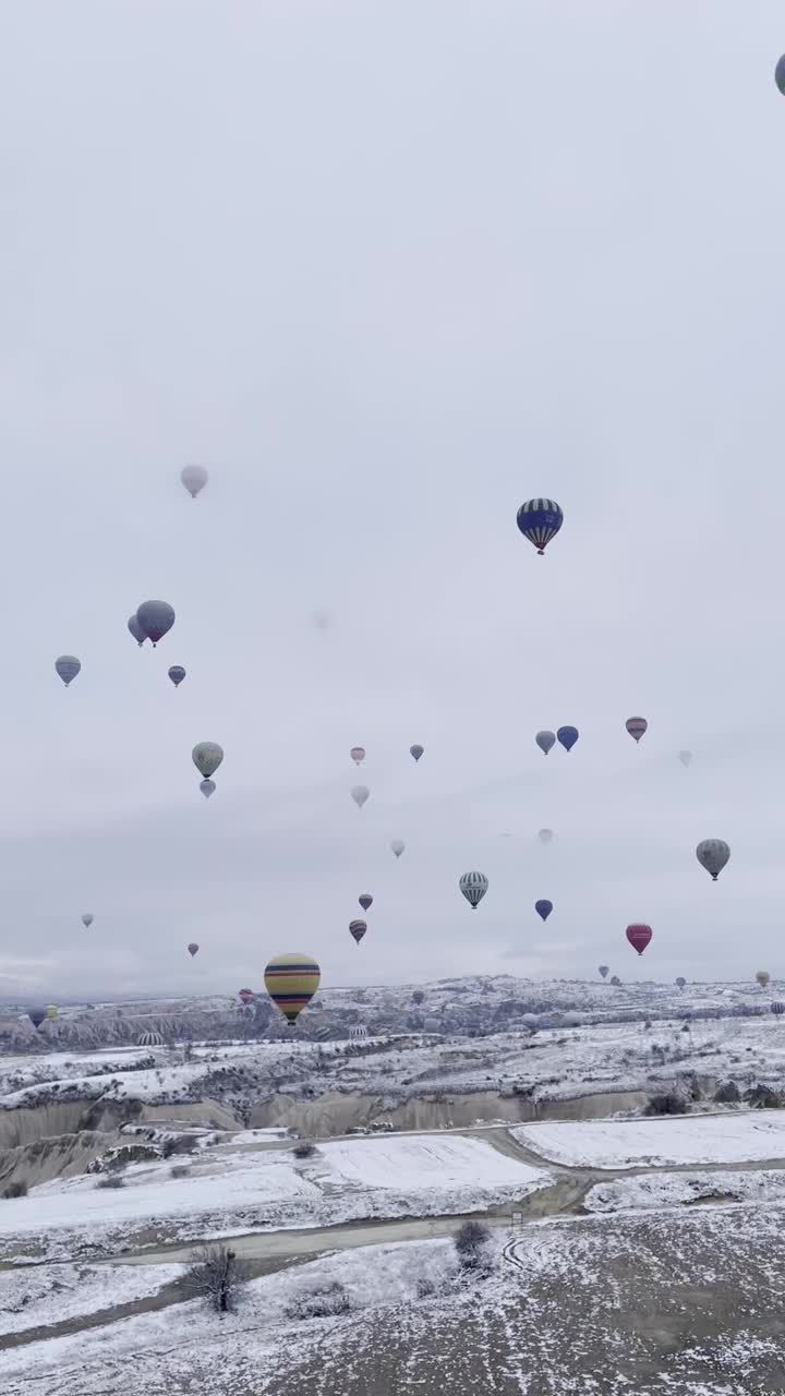 垂直拍摄的气球飞行在卡帕多西亚的小镇充满了冬天的雪视频下载