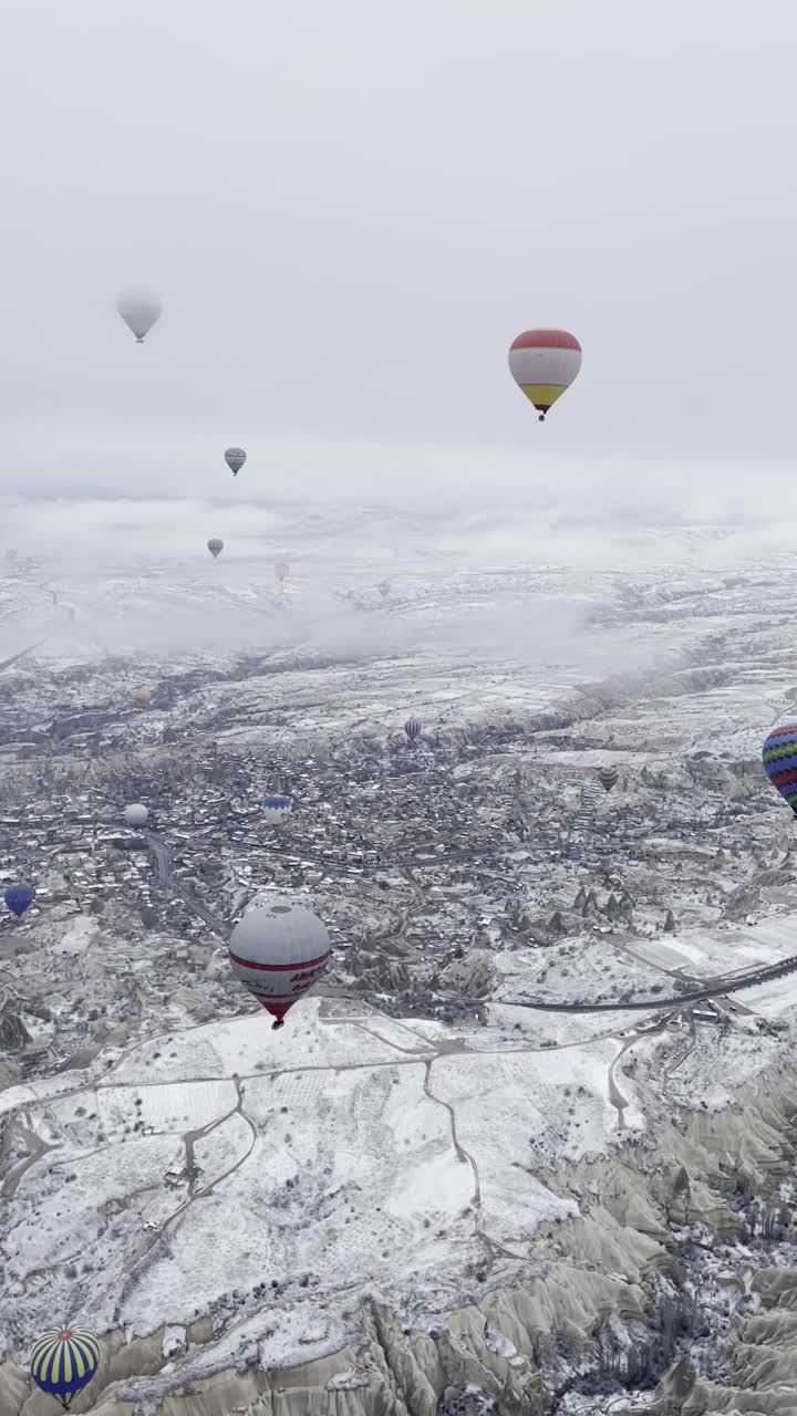 垂直拍摄的气球飞行在卡帕多西亚的小镇充满了冬天的雪视频下载