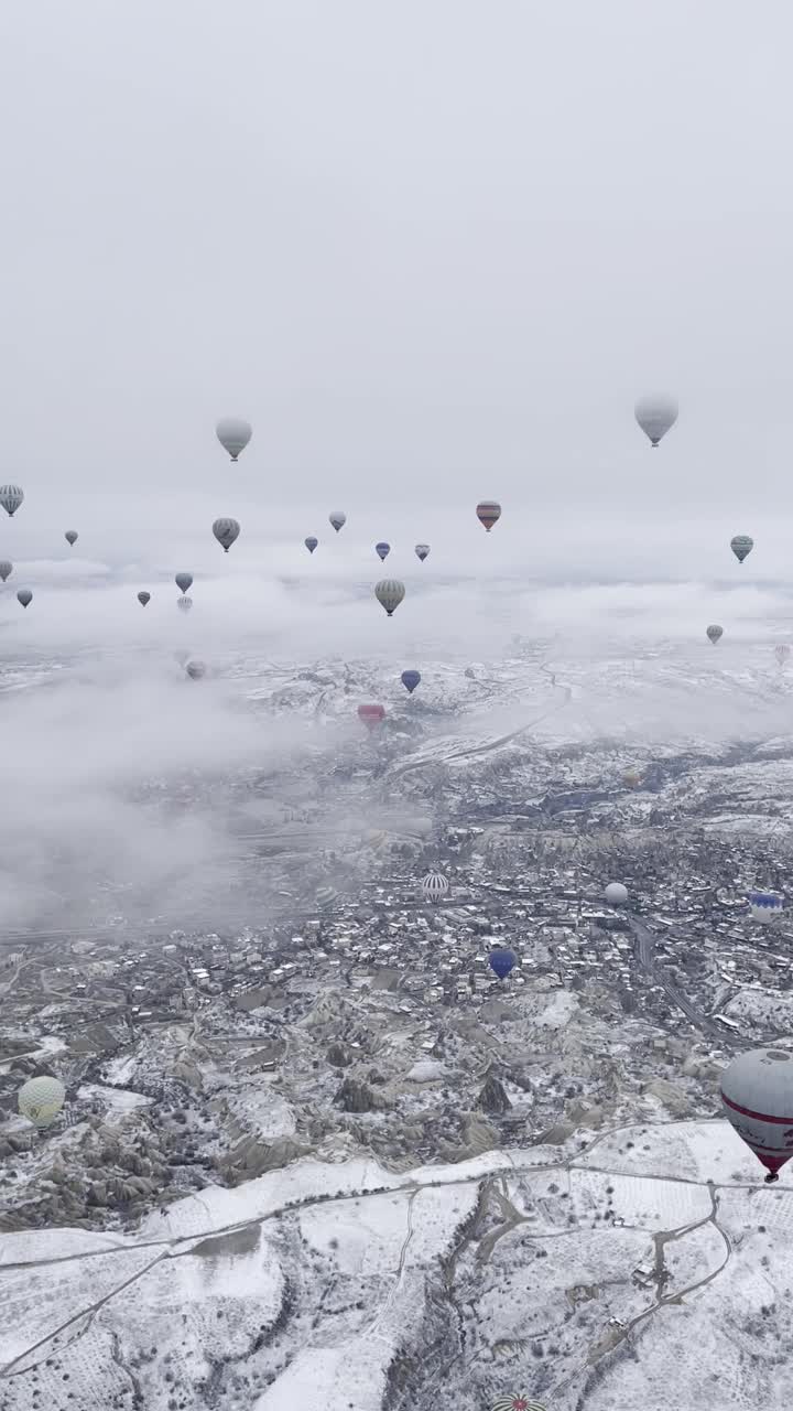 垂直拍摄的气球飞行在卡帕多西亚的小镇充满了冬天的雪视频下载