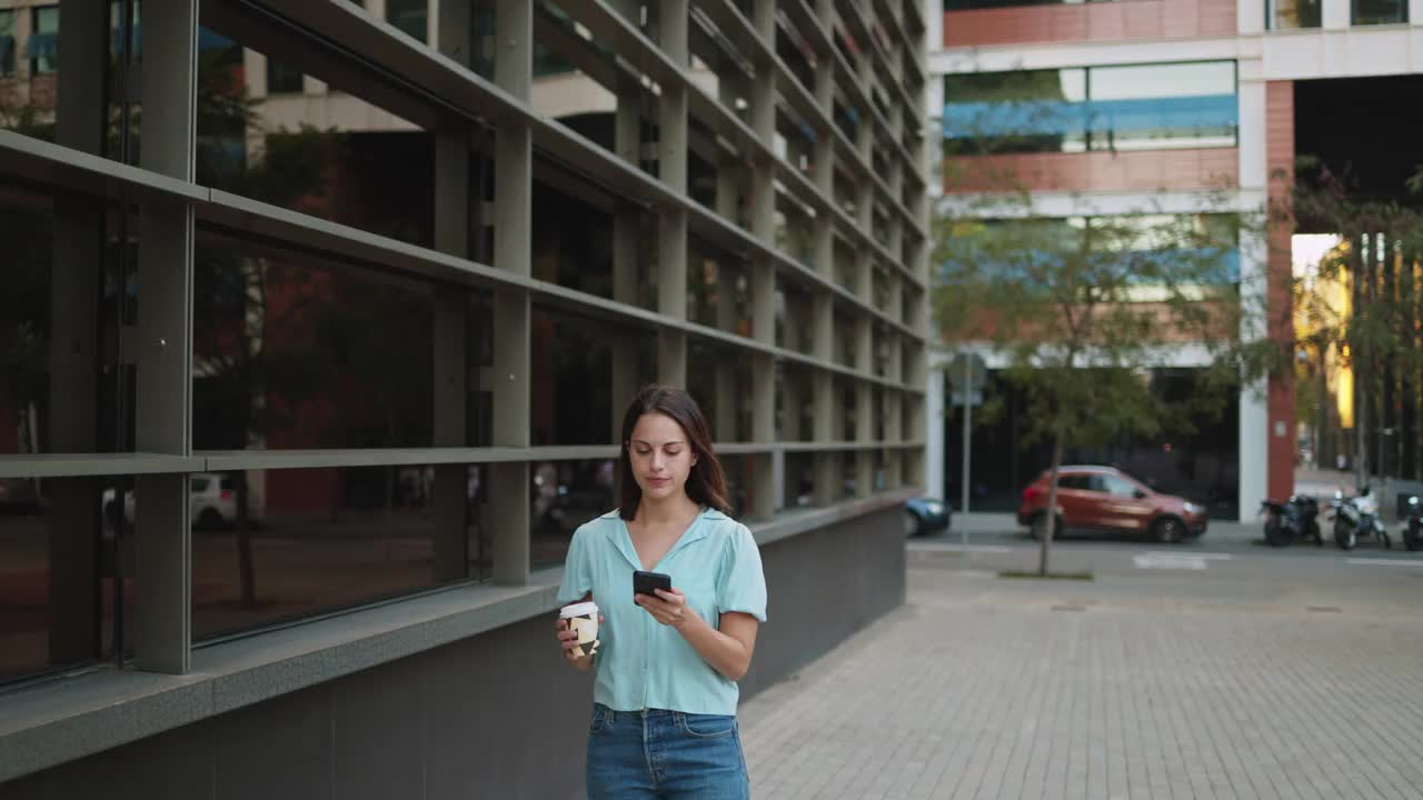 穿着便服的年轻女商人在办公室外拿着咖啡休息时玩着手机视频素材