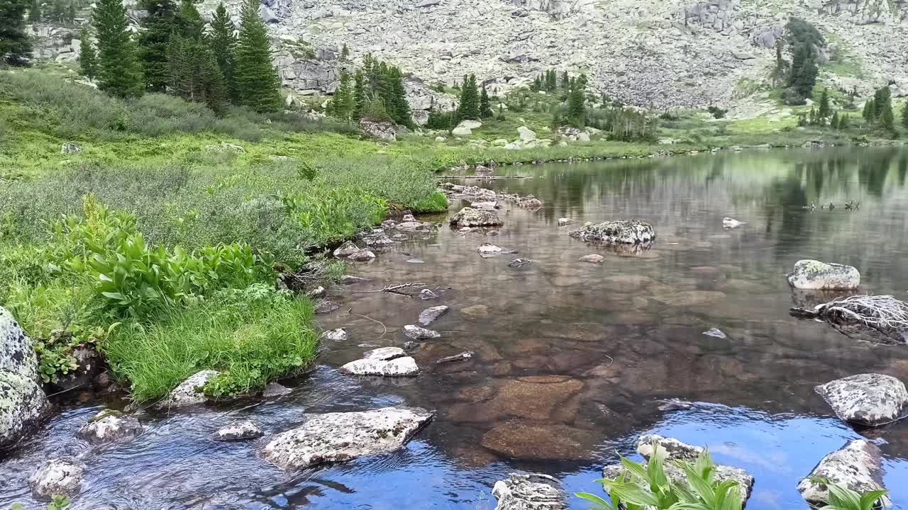 在一个多云的夏日，高山在一个小的山间湖泊平静的水面上的倒影。视频下载