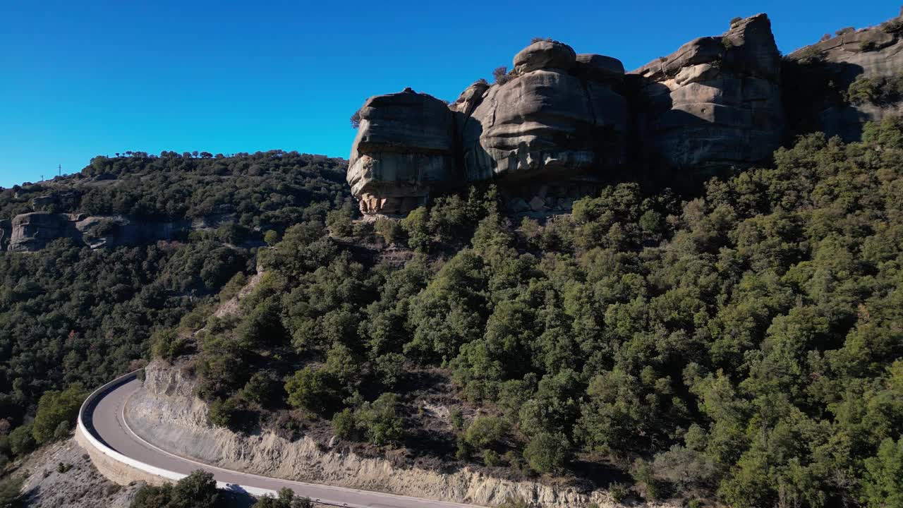 蜿蜒的道路穿过风景秀丽的Tavertet地区，在晴朗的天空下，有岩石悬崖和郁郁葱葱的绿色植物视频素材