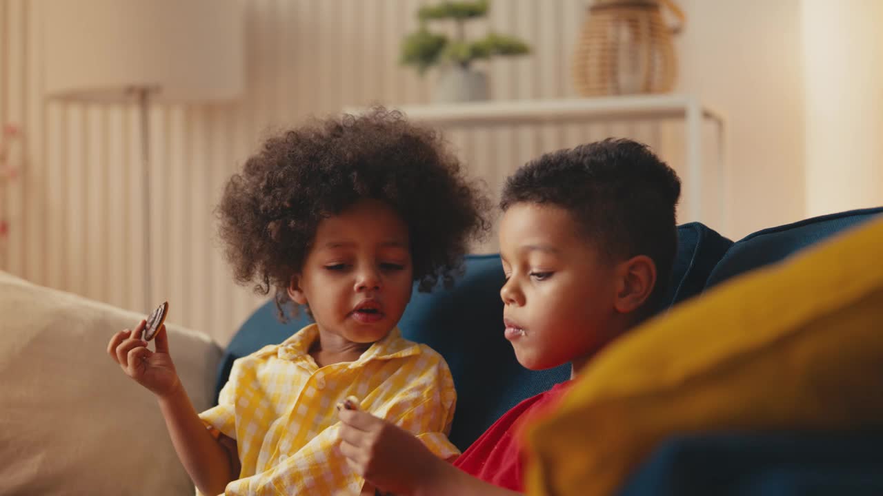 两个非裔美国小男孩坐在沙发上吃饼干，享受着甜食视频下载