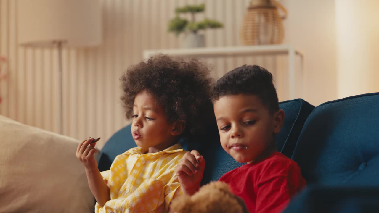 午餐时间，兴高采烈的非裔美国儿童坐在家里的沙发上吃饼干视频下载