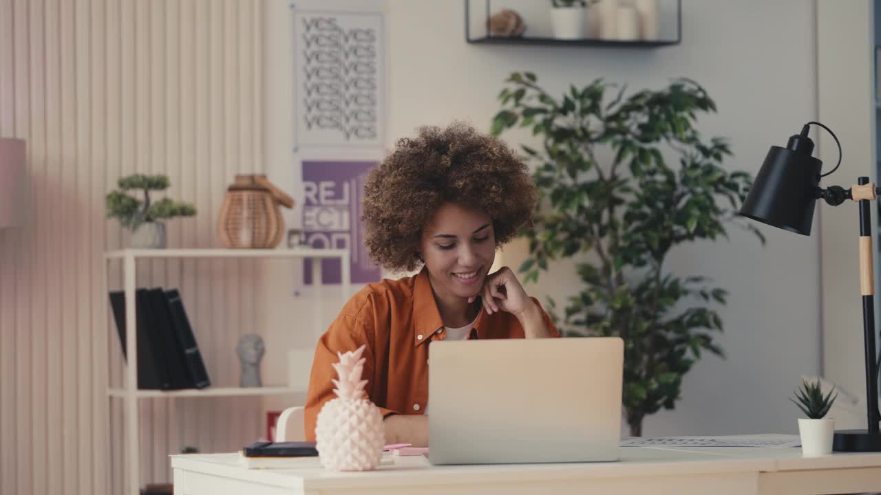 微笑的非裔美国女性在办公室用笔记本电脑工作，做着创造性的工作视频下载