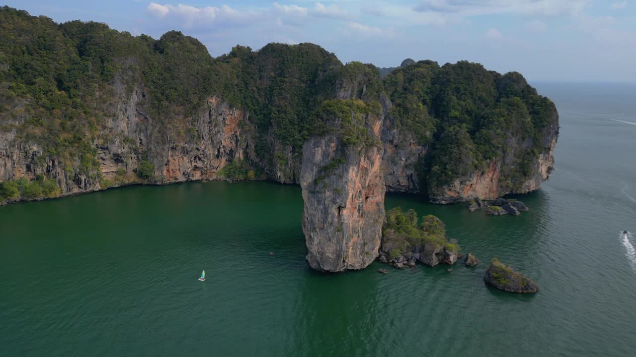 一个幽静的海湾，绿松石般的水，周围是高耸的悬崖，覆盖着郁郁葱葱的绿色植被。可爱的鸟瞰图飞行宽轨道概述无人机视频素材