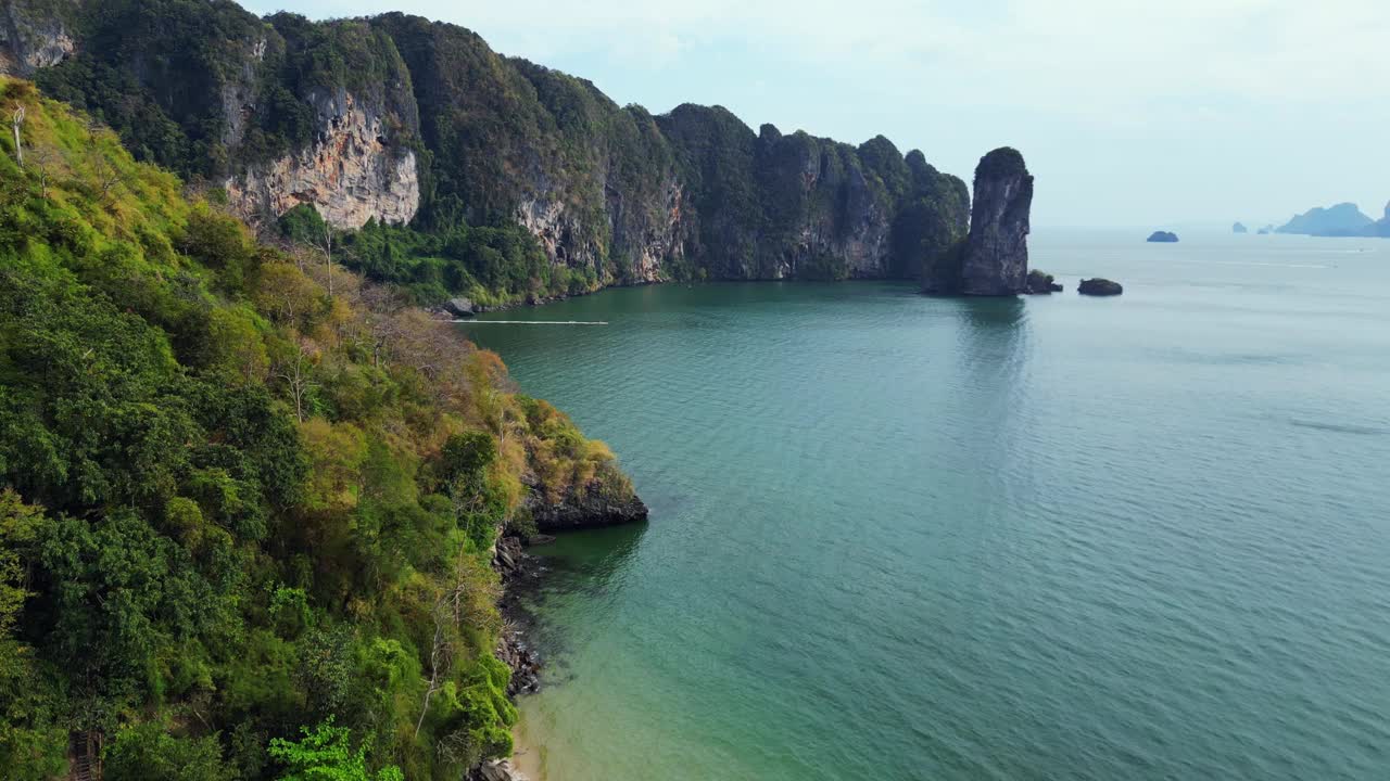 一个幽静的海湾，绿松石般的水，周围是高耸的悬崖，覆盖着郁郁葱葱的绿色植被。完美的鸟瞰图飞行下降无人机视频素材