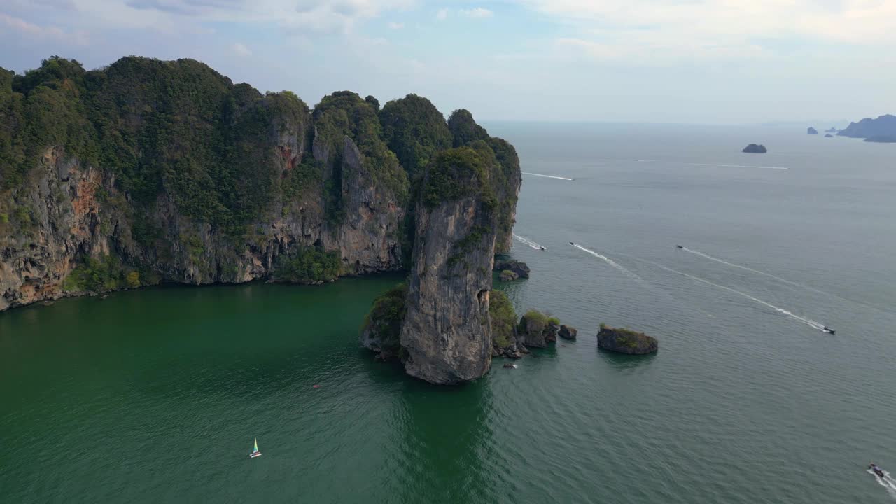 一个幽静的海湾，绿松石般的水，周围是高耸的悬崖，覆盖着郁郁葱葱的绿色植被。平稳的鸟瞰图飞行反向飞行无人机视频素材