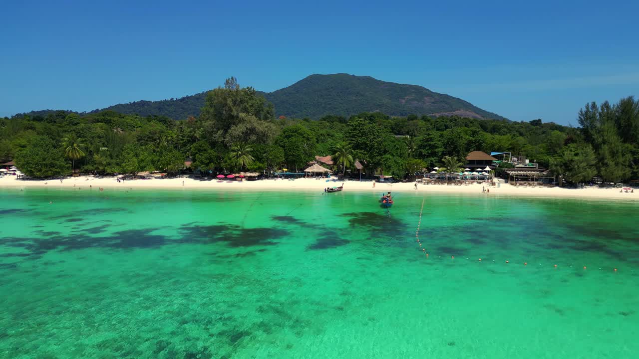 游客们在热带岛屿海滩上享受阳光明媚的一天，传统的泰国长尾船停泊在碧绿的海水中。令人难以置信的鸟瞰图飞行全景概述无人机视频素材