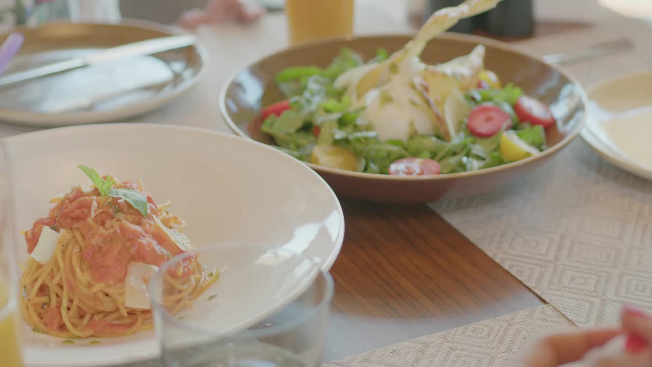 在昂贵的豪华饭店的餐厅里，一家人坐在餐桌旁。沙拉、意大利面、装有果汁和鸡尾酒的酒杯都在桌子上视频素材