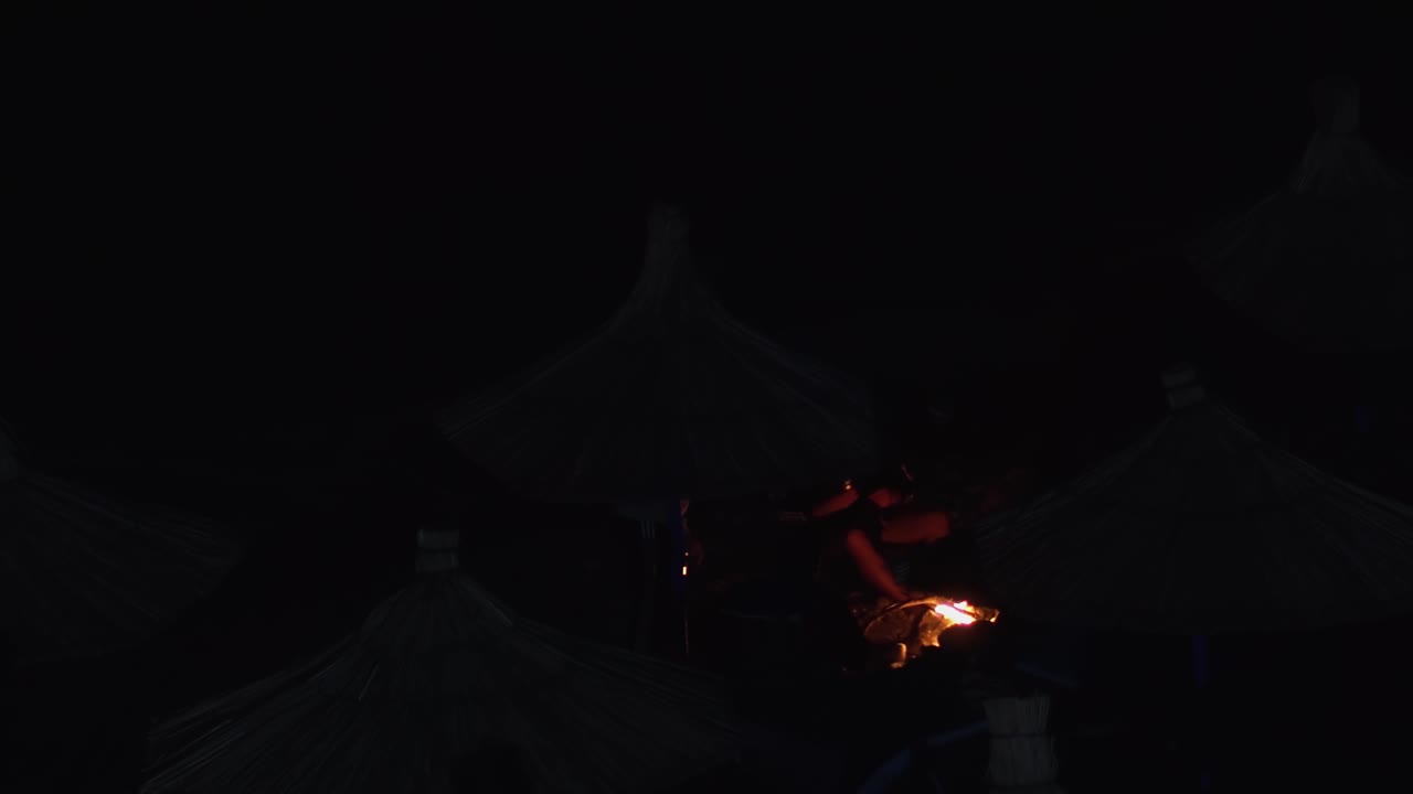 一个人拿着点燃的火炬坐在夜晚的海滩上。这个场景黑暗而神秘，人的剪影映衬着帐篷和发光的火炬，营造出一种怪异的气氛视频下载